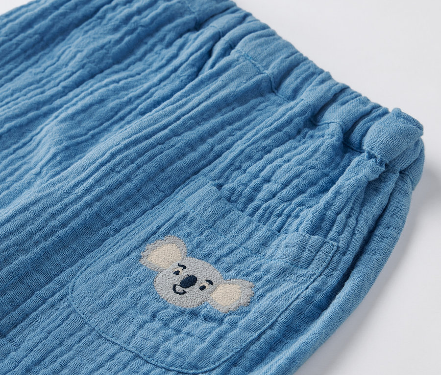 Gros plan sur un pantalon bouffant en mousseline bleue pour bébé avec une poche et une broderie koala.
