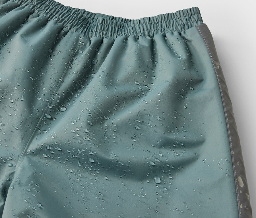 Détail d'un pantalon de pluie pour enfant, sauge, avec des gouttes d'eau.