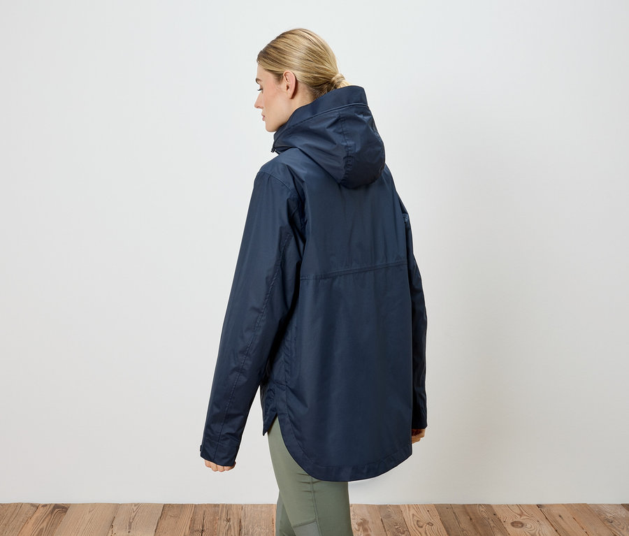 Vue arrière d'une femme blonde portant un manteau de pluie bleu marine à capuche et un pantalon vert.