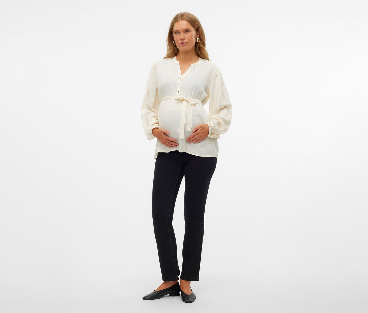 Femme enceinte portant un top MAMALICIOUS « MLMERCY LIA », un pantalon noir et des ballerines, les mains sur le ventre.