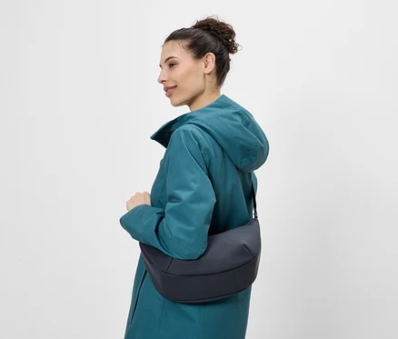 Femme de profil portant un sac à bandoulière bleu marine et un imperméable bleu pétrole.