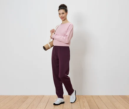 Femme portant un pull rose avec un tapis de yoga sur l'épaule.