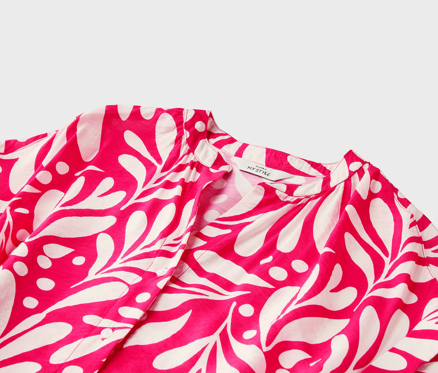 Gros plan sur un chemisier rose à imprimé de feuilles blanches et à encolure en V.