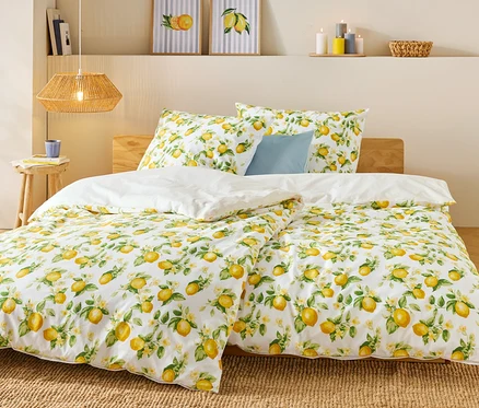 Lit avec motif citron, couette blanche et coussin bleu. Une tasse et des livres sont posés sur la table de chevet.