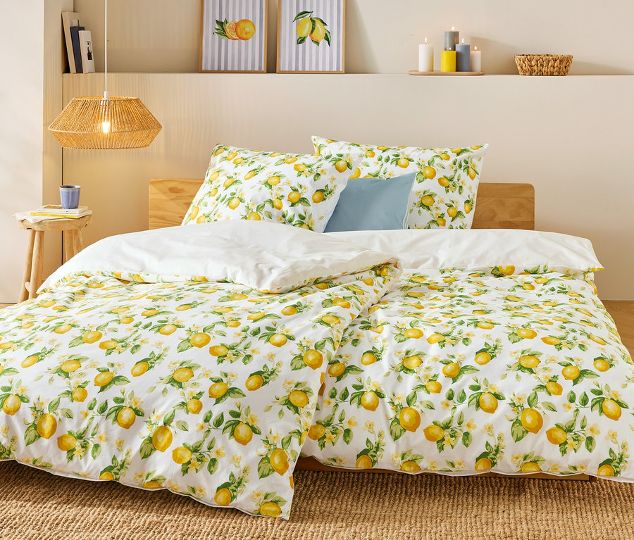 Lit avec motif citron, couette blanche et coussin bleu. Une tasse et des livres sont posés sur la table de chevet.