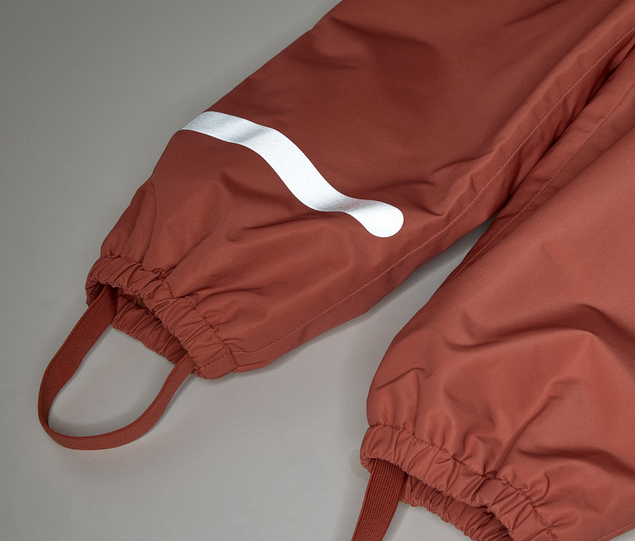 Gros plan sur deux jambes de pantalon couleur rouille avec poignets élastiques et réflecteurs blancs.
