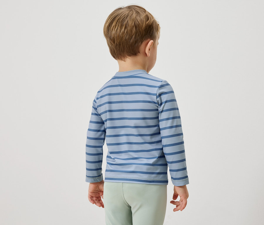 Un enfant vu de dos, portant un t-shirt à manches longues rayé bleu et un pantalon vert clair.