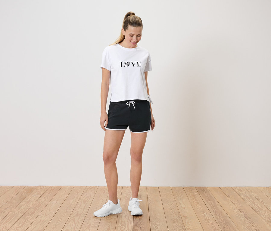 Femme debout portant un t-shirt blanc avec l'inscription LOVE et un short noir avec des accents blancs.
