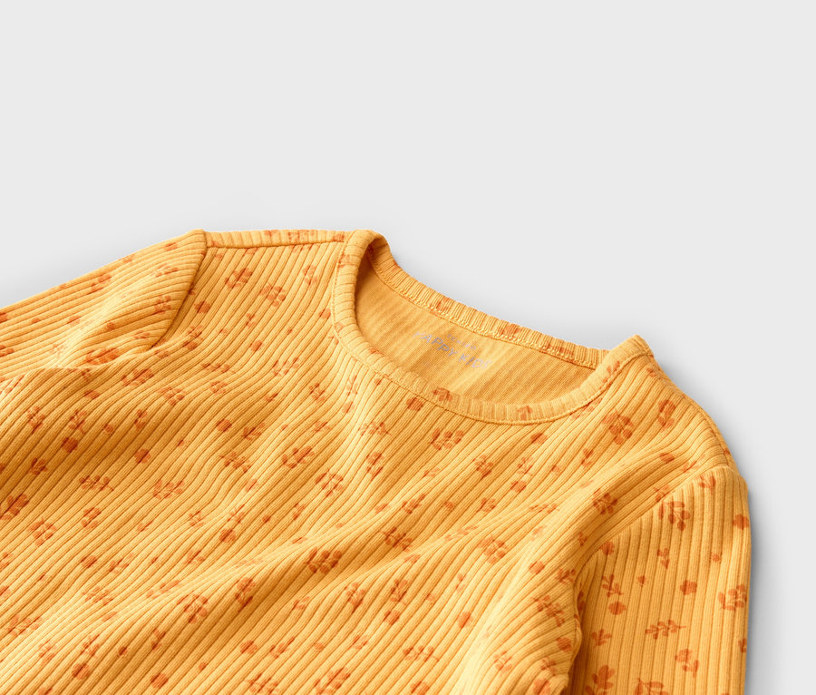 Gros plan d'un haut à manches longues jaune côtelé avec un motif floral orange sur fond gris.