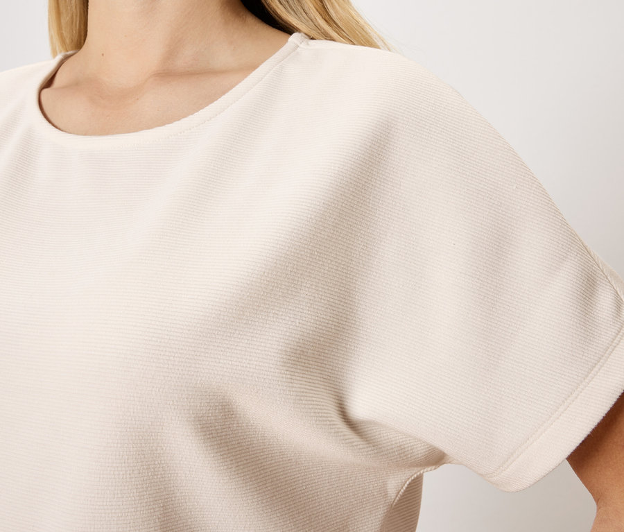 Gros plan d'une femme portant un haut beige clair à manches courtes et à col rond.