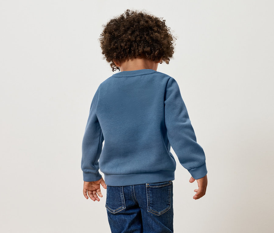 Vue arrière d'un enfant aux cheveux bouclés portant un pull bleu et un jean.