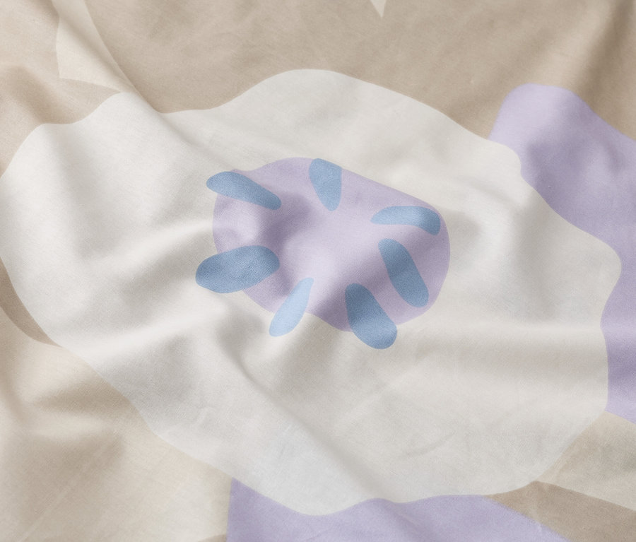 Gros plan d'une literie froissée avec un grand motif floral en blanc, violet et beige.