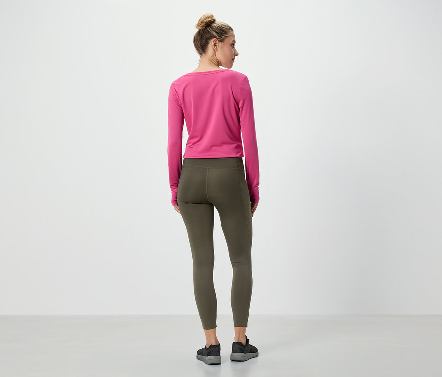 Une femme se tient dos à la caméra, portant un haut rose à manches longues et un legging vert olive.