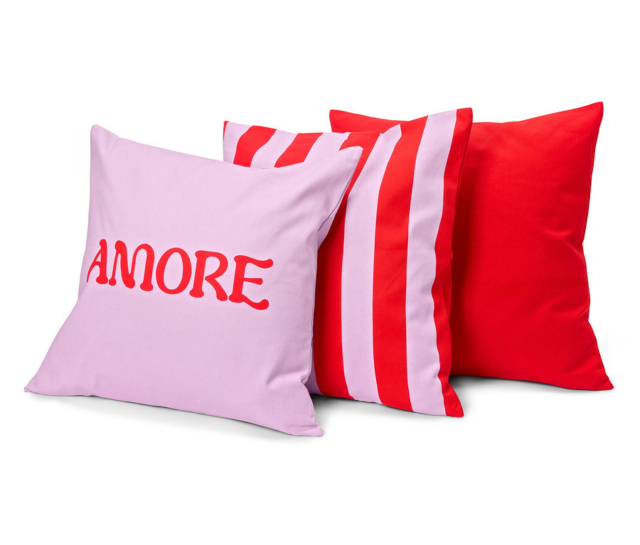 Trois coussins : un lilas avec le mot rouge « AMORE », un rayé, rouge et lilas et un rouge uni.