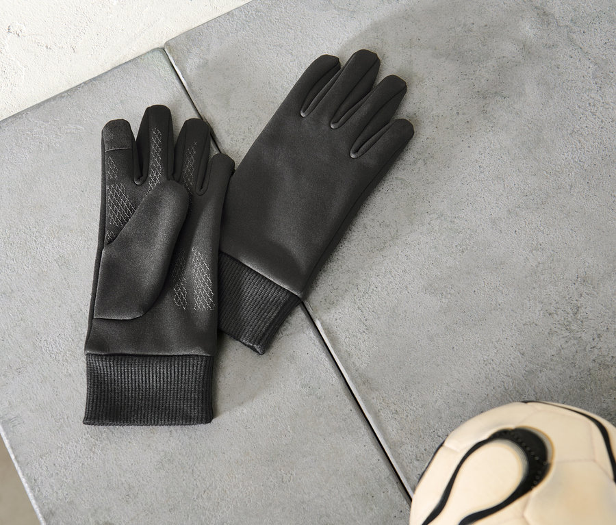 Une paire de gants noirs et un ballon de football posés sur une surface grise.
