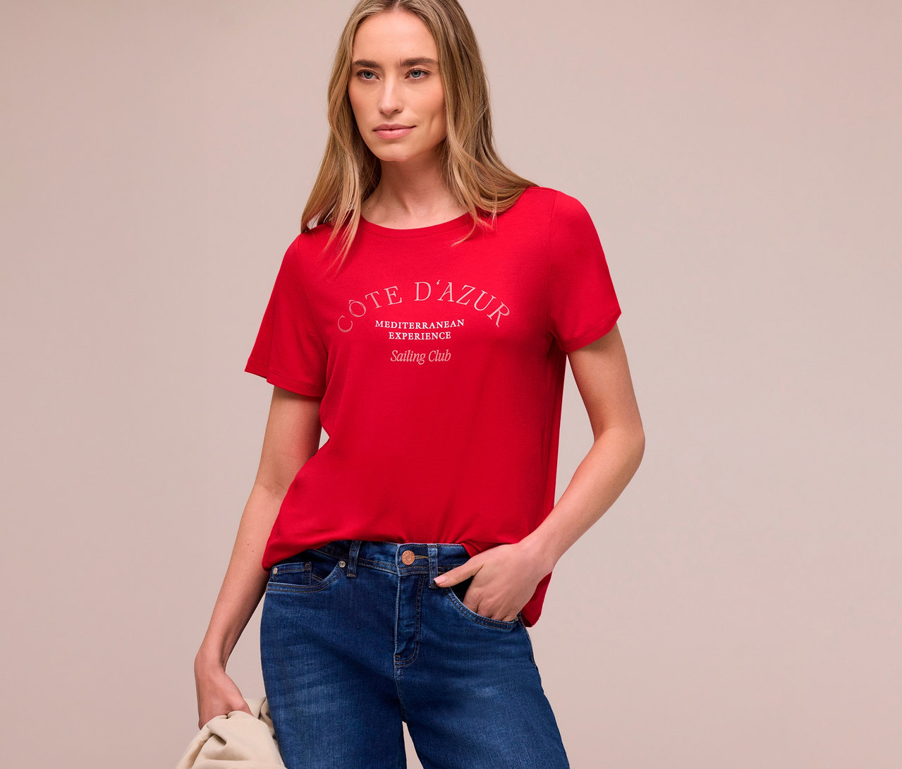 Femme portant un t-shirt Street One rouge et un jean, avec une veste beige sur le bras.