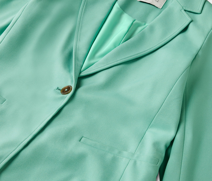 Gros plan d'un blazer vert menthe avec un bouton et des poches