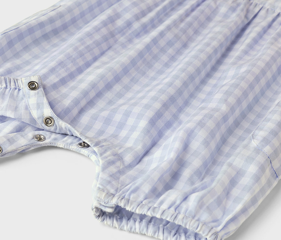 Gros plan sur une barboteuse à carreaux bleu et blanc avec boutons-pression.