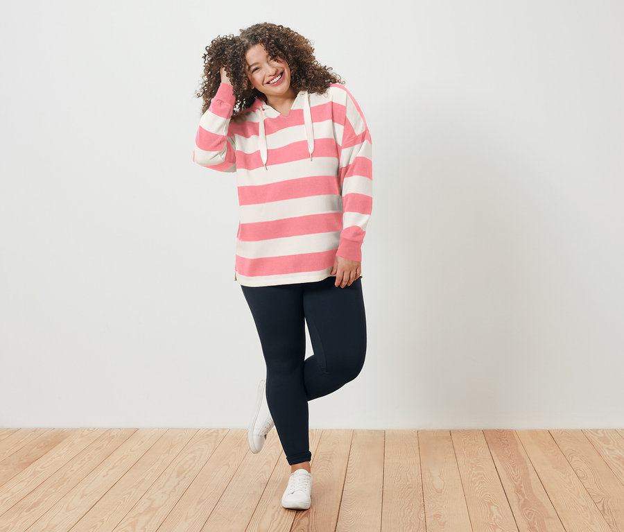Femme aux cheveux bouclés portant un sweat à capuche rayé et des leggings, souriant.