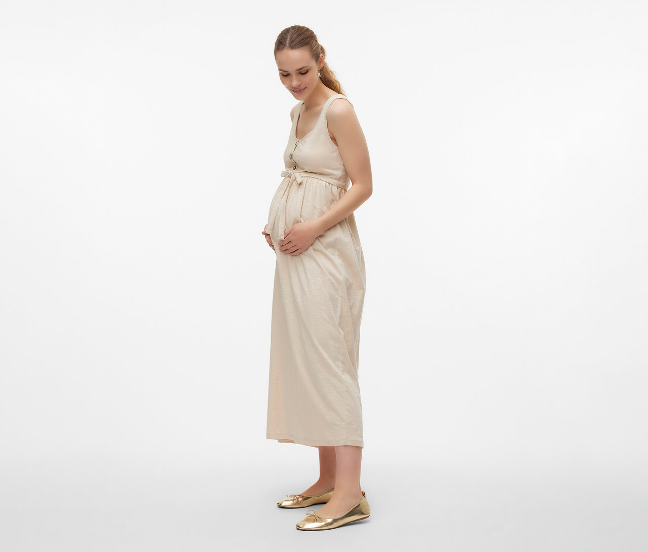 Femme enceinte portant une robe de grossesse MAMALICIOUS «
MLEVI LIA » avec ceinture et chaussures dorées.
