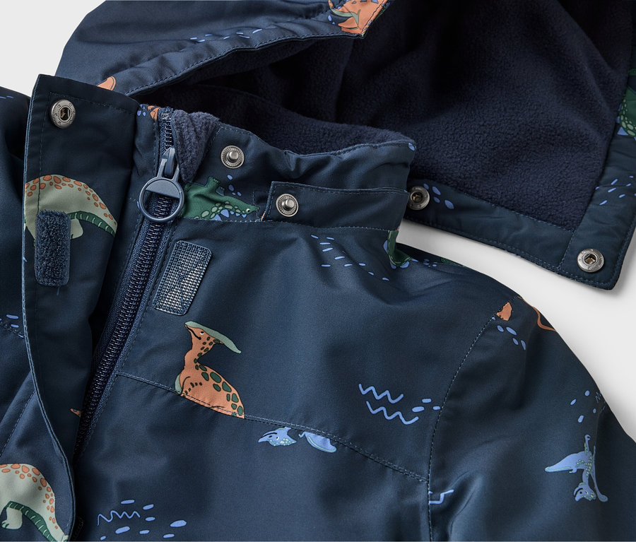 Gros plan d'une veste bleu marine à motifs de dinosaures, avec fermeture éclair et capuche doublée de polaire bleu marine.