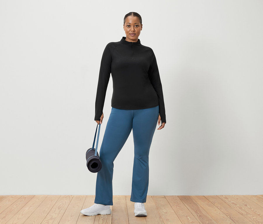Femme en haut noir et pantalon bleu tenant un tapis de yoga.