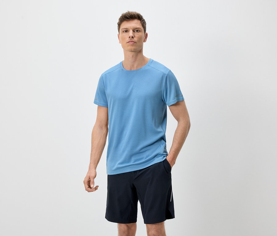 Homme portant un t-shirt bleu et un short noir sur fond blanc.