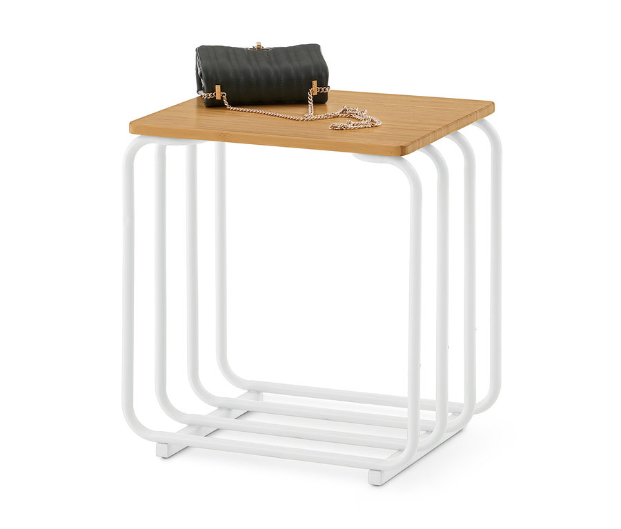 Un sac à main matelassé noir avec une chaîne dorée repose sur une table d'appoint carrée avec un plateau en bois clair et un cadre en métal blanc.