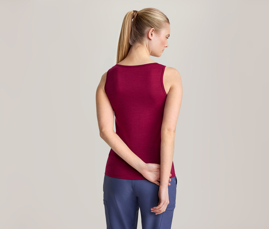 Femme de dos portant un débardeur bordeaux et un pantalon bleu, les mains croisées derrière le dos.
