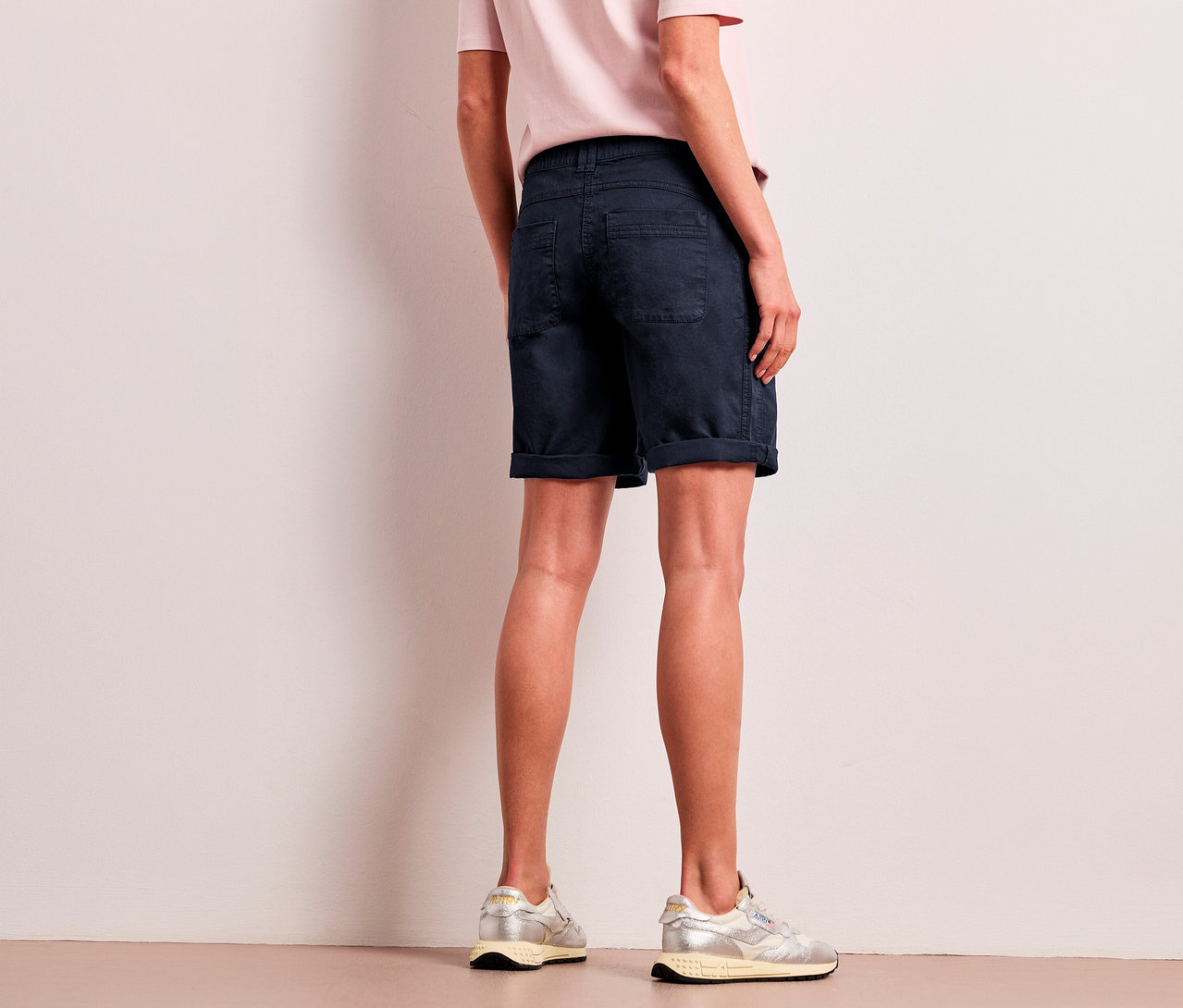 Une personne de dos porte un t-shirt rose clair, un bermuda Street One « Yulius » bleu marine et des baskets argentées.