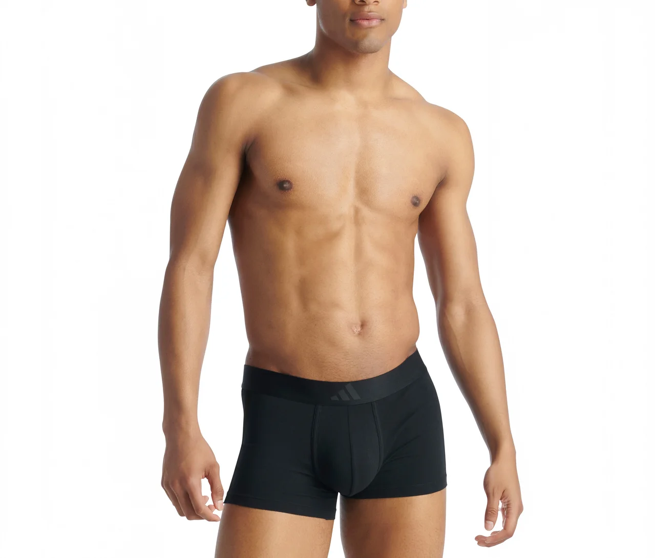 Homme torse nu à la peau foncée portant un boxer noir avec un logo Adidas visible sur la ceinture, debout devant un fond blanc.