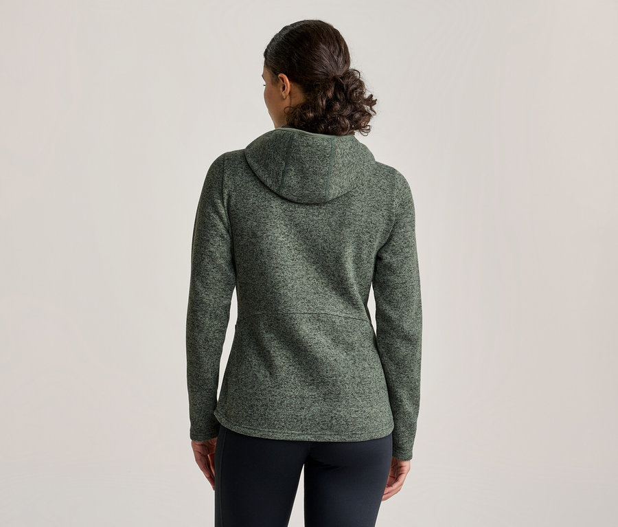 Femme vue de dos, portant une veste à capuche verte mouchetée et un pantalon noir.