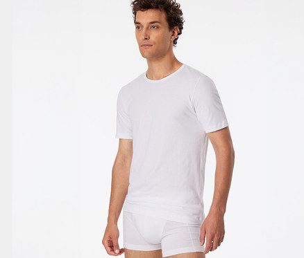 Homme aux cheveux bouclés portant un t-shirt SCHIESSER blanc et un boxer blanc.
