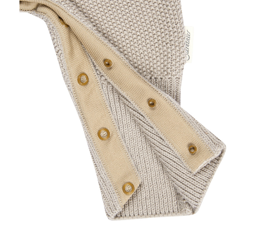 Gros plan d'un bonnet ou d'une cagoule tricotée beige clair, montrant deux sangles en tissu beige avec des boutons-pression marron. Une étiquette 'Sterntaler' est visible.