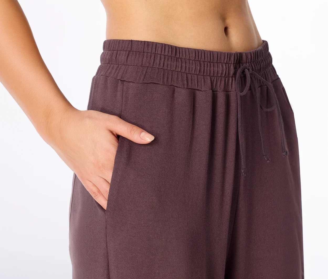 Gros plan d'une personne mettant sa main dans la poche d'un pantalon de jogging violet foncé avec taille élastique et cordon de serrage.
