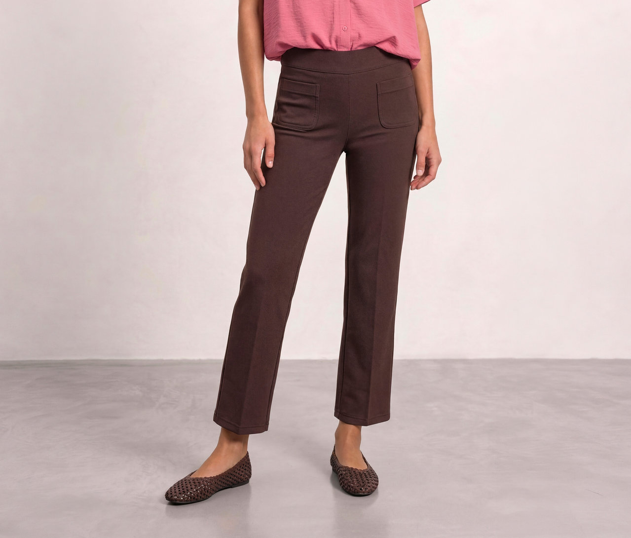 Une personne porte un pantalon en tissu Street One marron avec des poches avant, une chemise rose et des ballerines tressées marron.