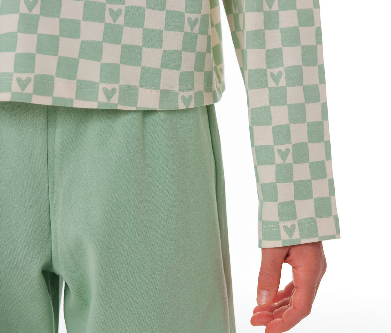 Enfant portant un Pyjama Interlock pour enfant SCHIESSER, avec un haut à carreaux vert clair et crème avec des cœurs et un pantalon vert clair uni.