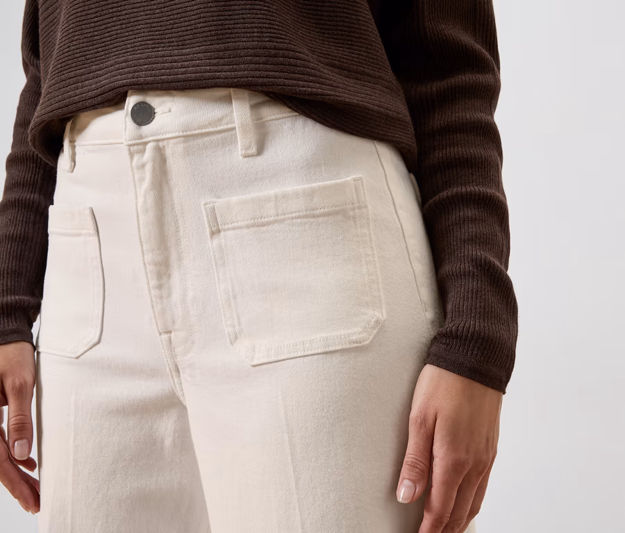Personne portant un Jean Wide Leg – Fit « Viki » de couleur claire avec des poches plaquées à l'avant et un haut côtelé marron foncé à manches longues.