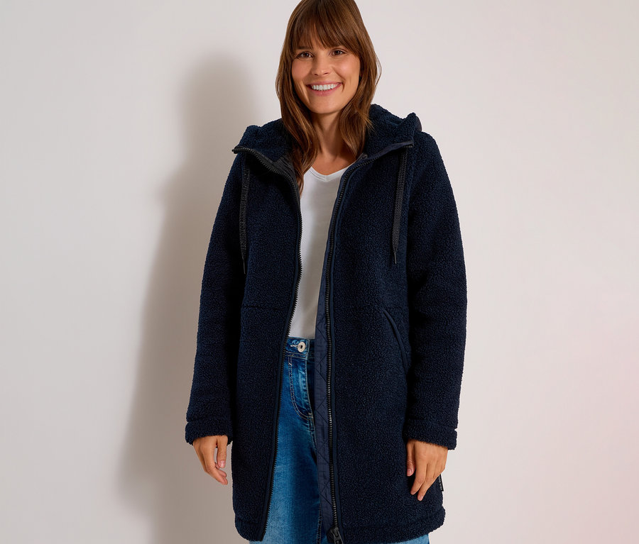 Femme souriante portant une veste CECIL bleu marine en polaire teddy ouverte, un t-shirt blanc et un jean.