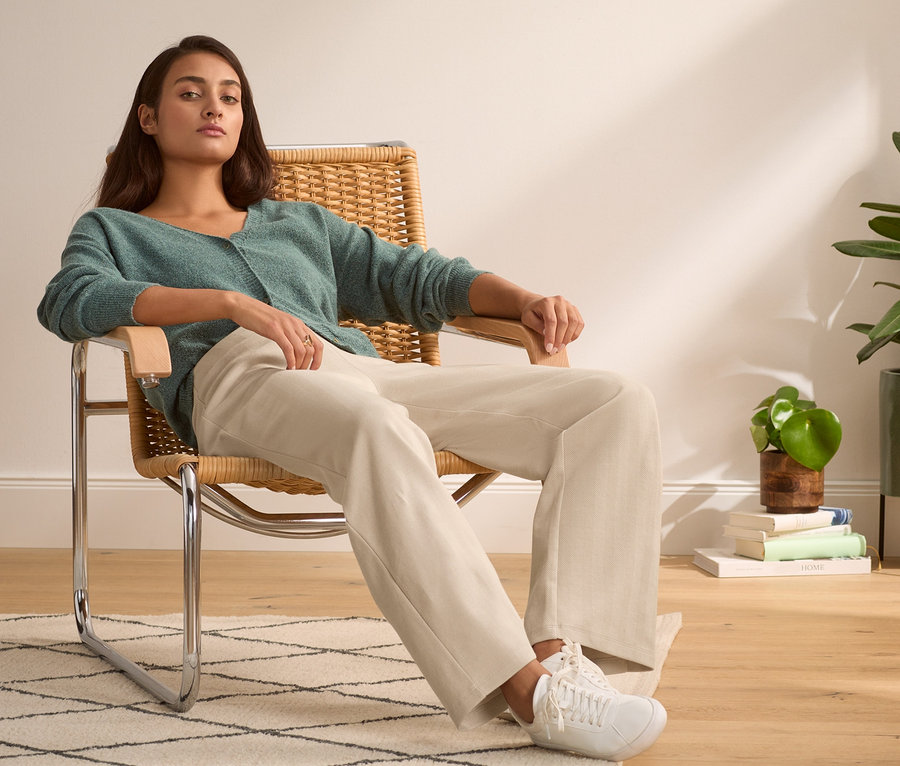 Femme assise dans un fauteuil portant un pull vert et un pantalon stretch.