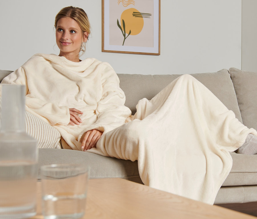 Une femme est assise sur un canapé et porte une couverture moelleuse avec des manches.