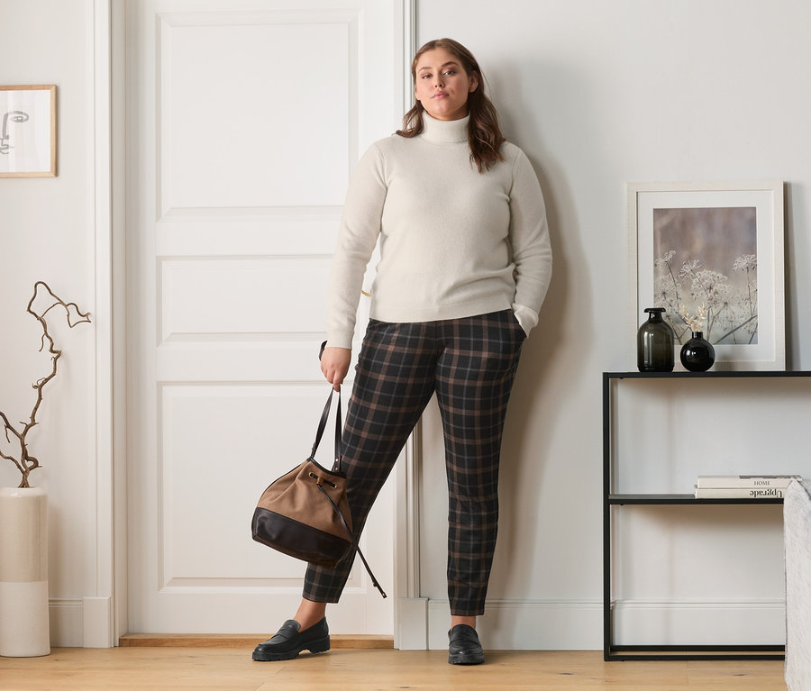 Femme posant en pull en maille fine en cachemire, pantalon de jogging à carreaux, mocassins en cuir et sac à bandoulière.