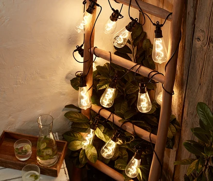 Une échelle enroulée d'une guirlande lumineuse avec ampoules LED à filament, à côté d'une boisson à la menthe.