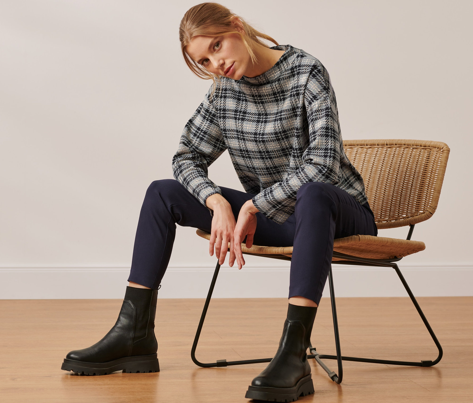 Une femme est assise sur une chaise en osier et porte un sweat-shirt à carreaux.