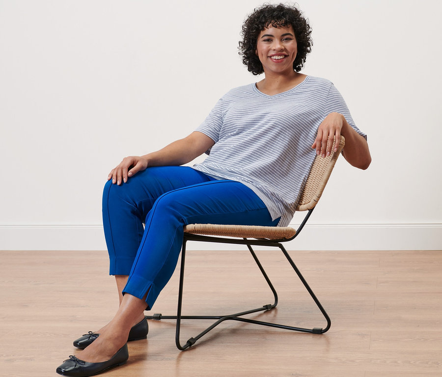 Femme assise sur une chaise portant un pantalon stretch bleu cobalt et un t-shirt rayé.