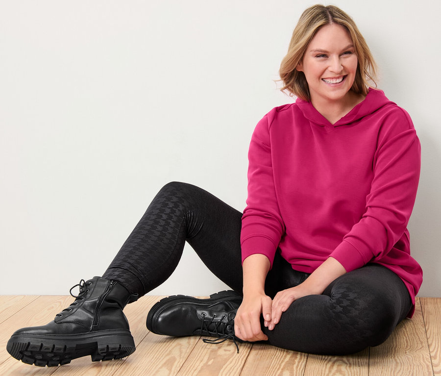 Femme assise sur un plancher en bois portant un pull à capuche rose en mélange de modal et un legging thermique noir avec relief.