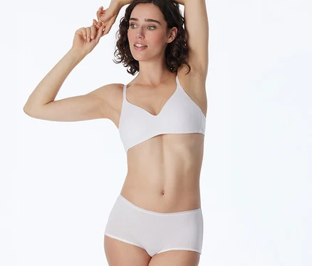 Femme portant un short SCHIESSER blanc et un soutien-gorge blanc, les bras levés au-dessus de la tête.