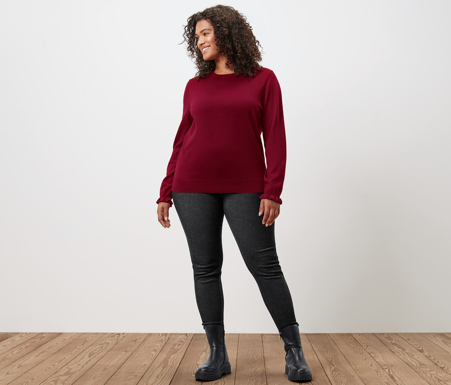 Femme posant dans un pull en maille fine rouge foncé avec poignets ruchés et un legging doublé à l’aspect jean.