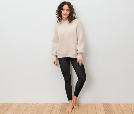 Une femme debout porte un legging thermique et un pull.