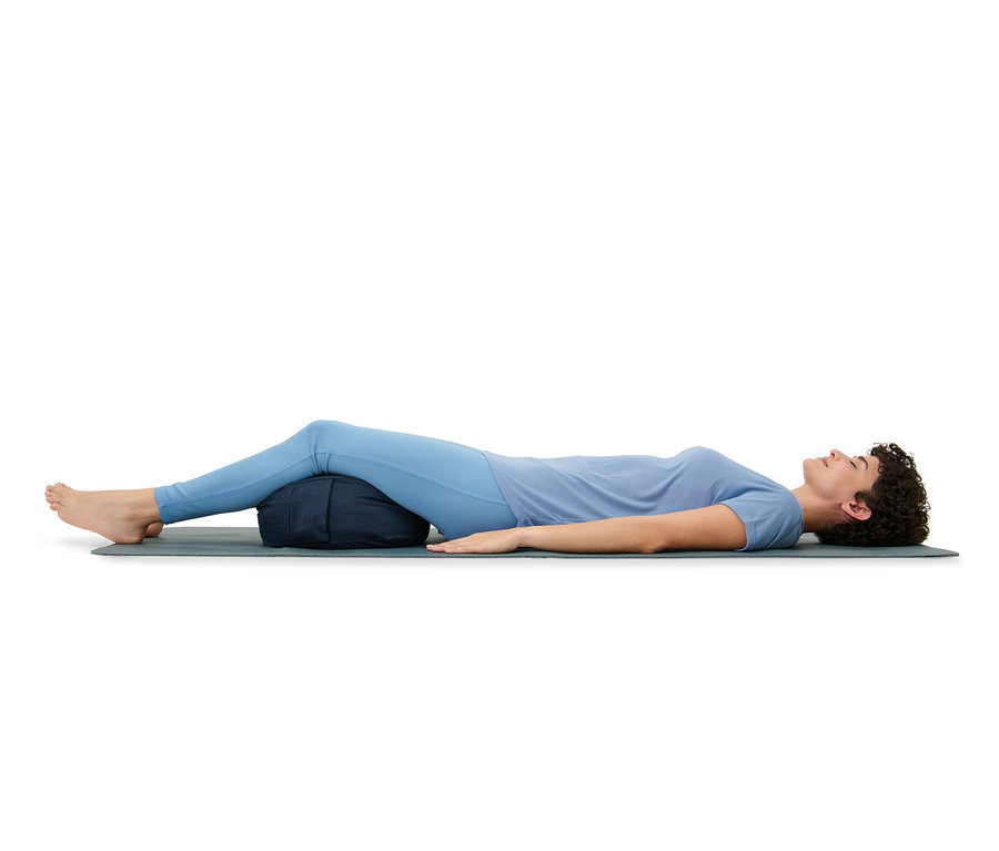 Femme allongée sur un tapis, les jambes sur un coussin de méditation.